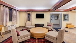 A hotel room with a round coffee table surrounded by four armchairs, a flat-screen TV mounted on the wall, and a large window with curtains. - La Quinta Inn & Suites by Wyndham Helena (Helena)