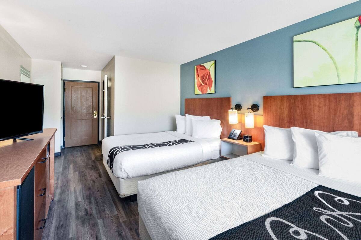 A hotel room with two beds, a TV, a wooden desk, and a nightstand with lamps.