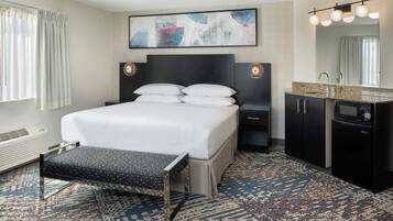 A hotel room with a bed, bedside tables, a bench, a large mirror, and a wall-mounted artwork.
