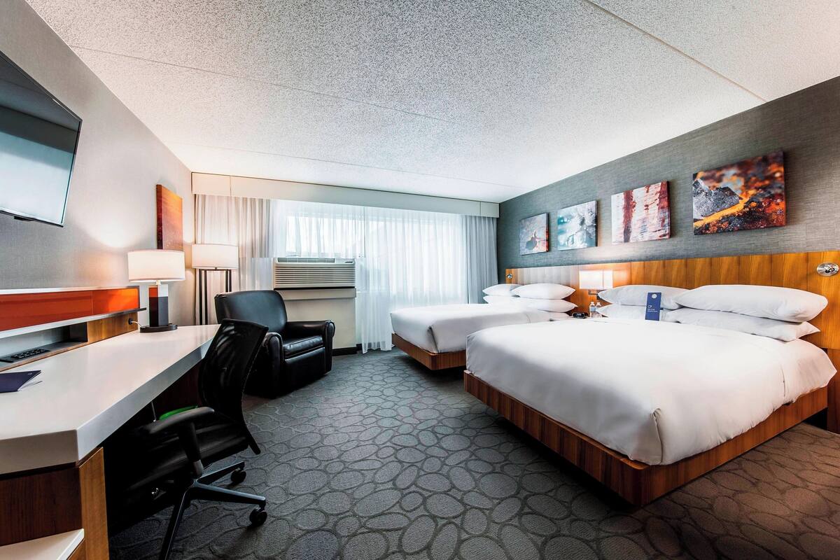 Une chambre d’hôtel équipée d’un bureau, de deux lits, d’une télévision et d’œuvres d’art accrochées au mur.