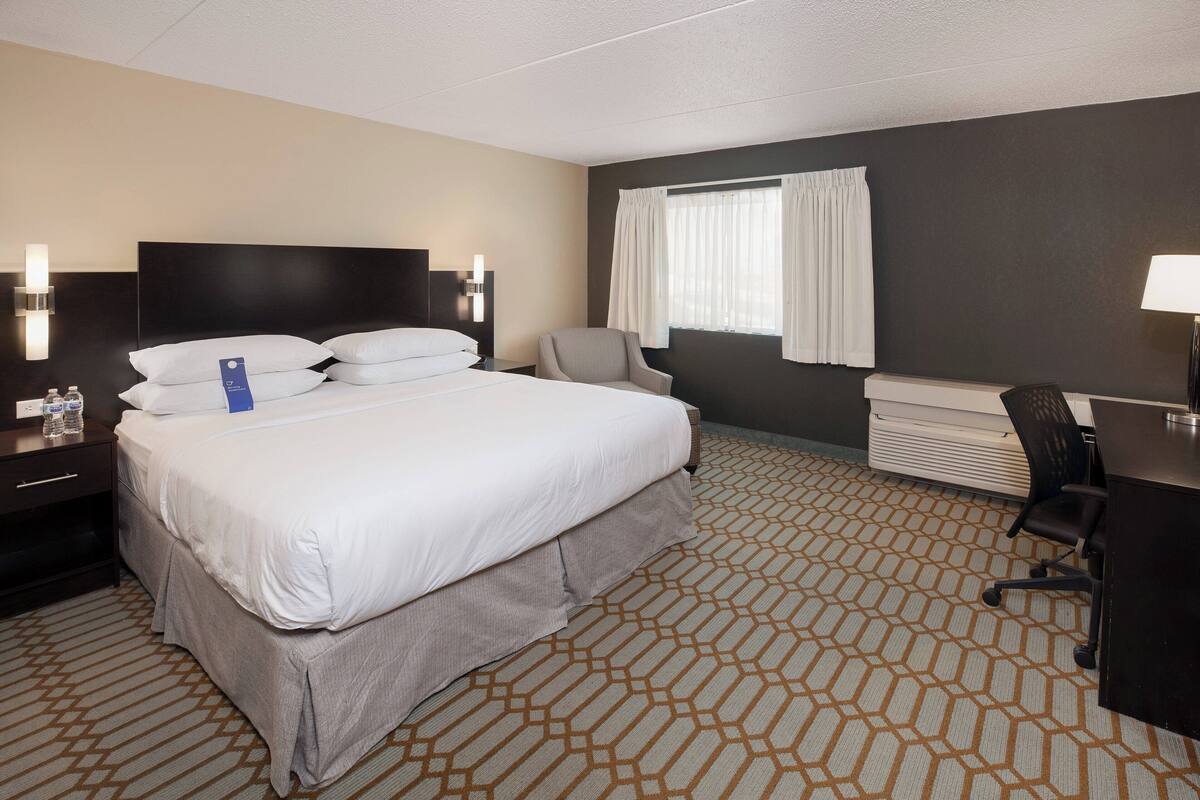 Une chambre d’hôtel avec un grand lit, un bureau, une chaise et une fenêtre avec des rideaux.