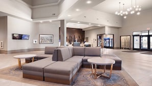 A spacious lobby with a large sectional sofa, two round tables, and a modern chandelier.