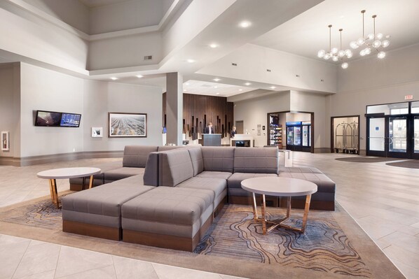 A spacious lobby with a large sectional sofa, two round tables, and a modern chandelier.