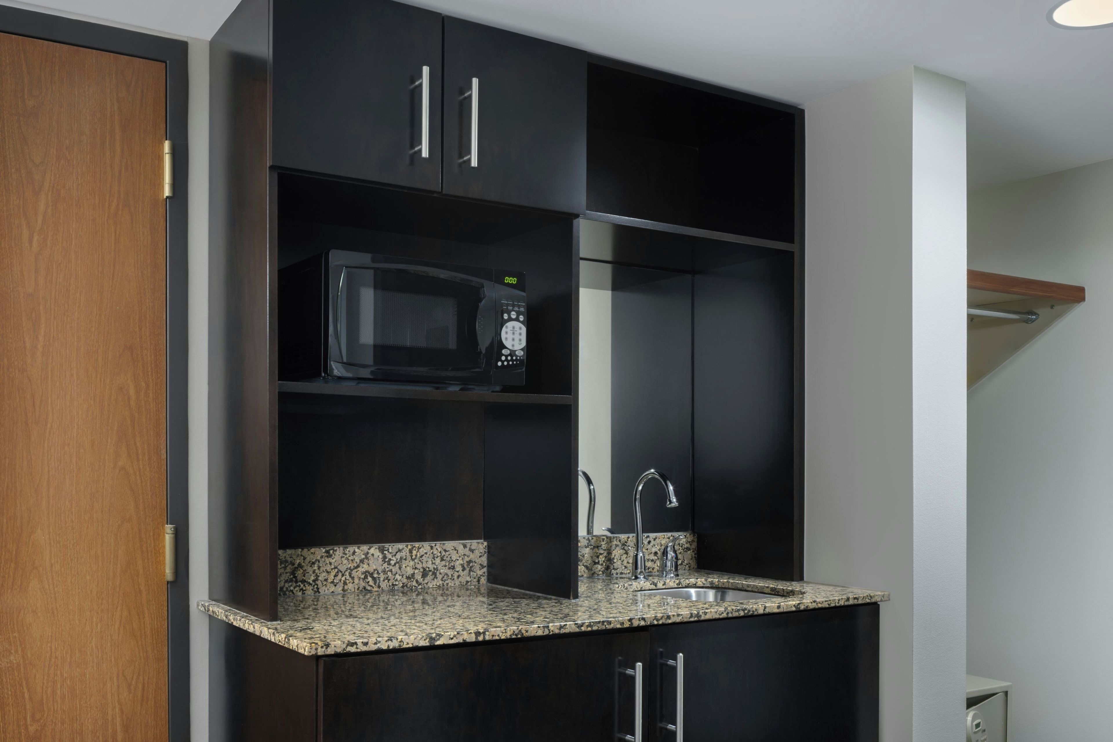 A kitchen with dark cabinetry, a granite countertop, a stainless steel sink, and a microwave.