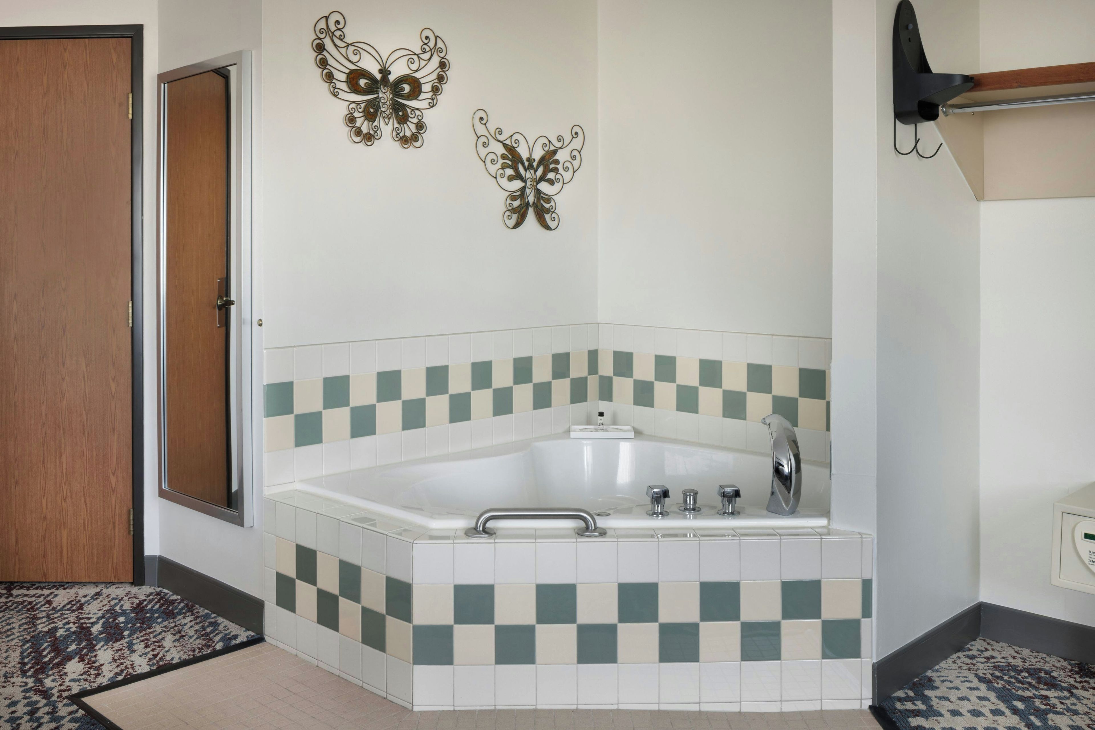 A bathroom with a white bathtub, checkered tiles, and two butterfly wall decorations.