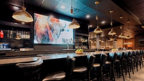 A bar area with leather bar stools, pendant lighting, and a large screen displaying an image.
