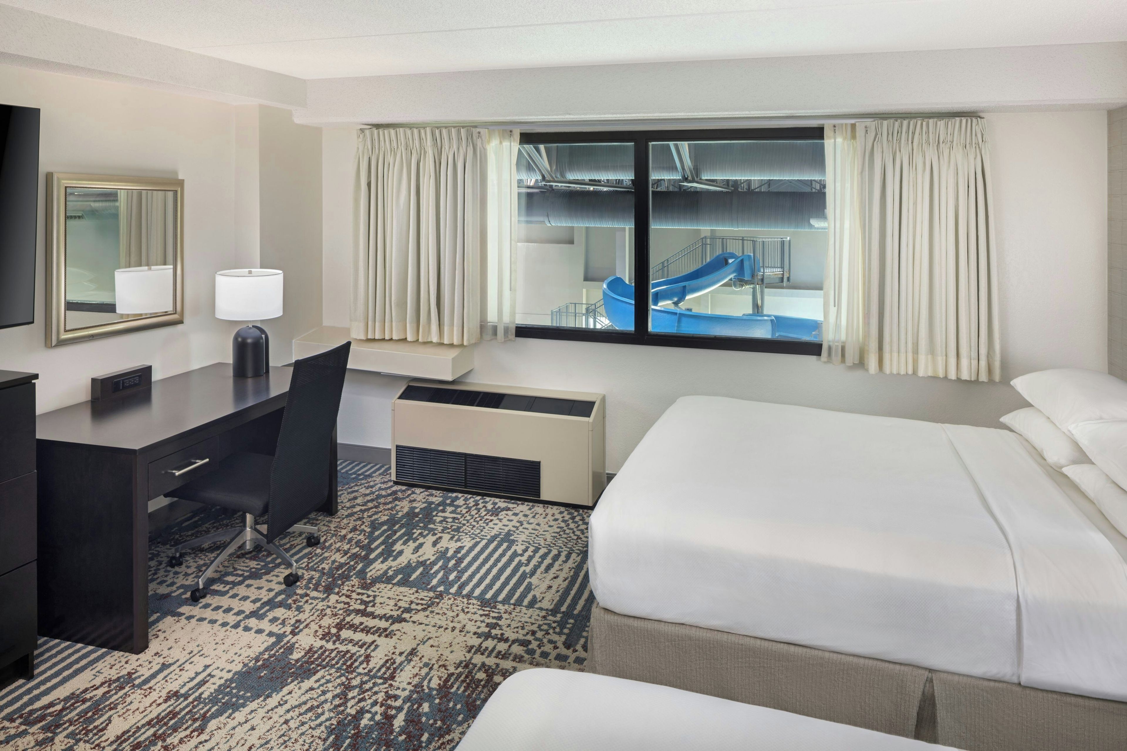 A hotel room with a bed, desk, chair, and a view of a water slide.