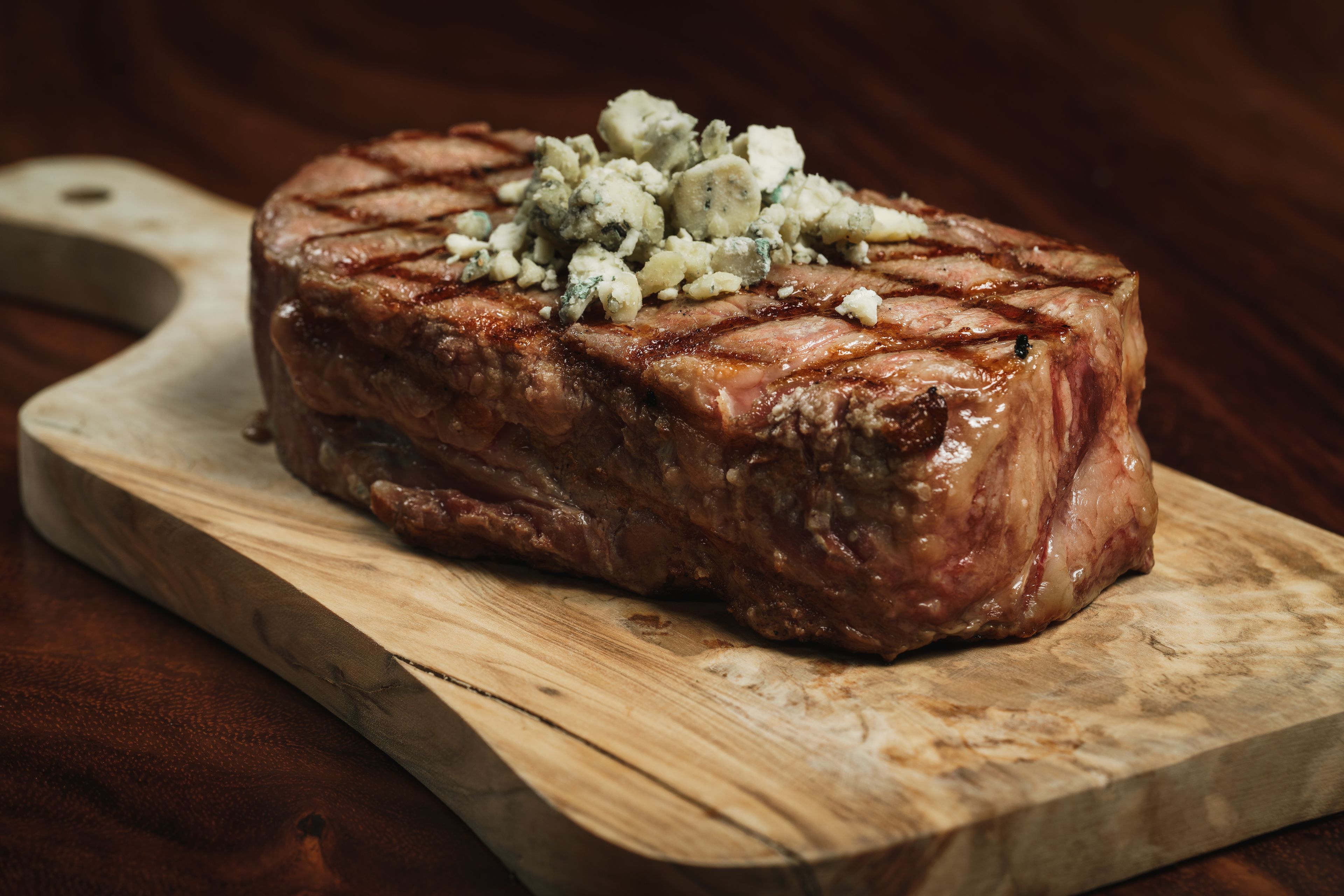 Un steak nappé de fromage bleu, présenté sur une planche à découper en bois.