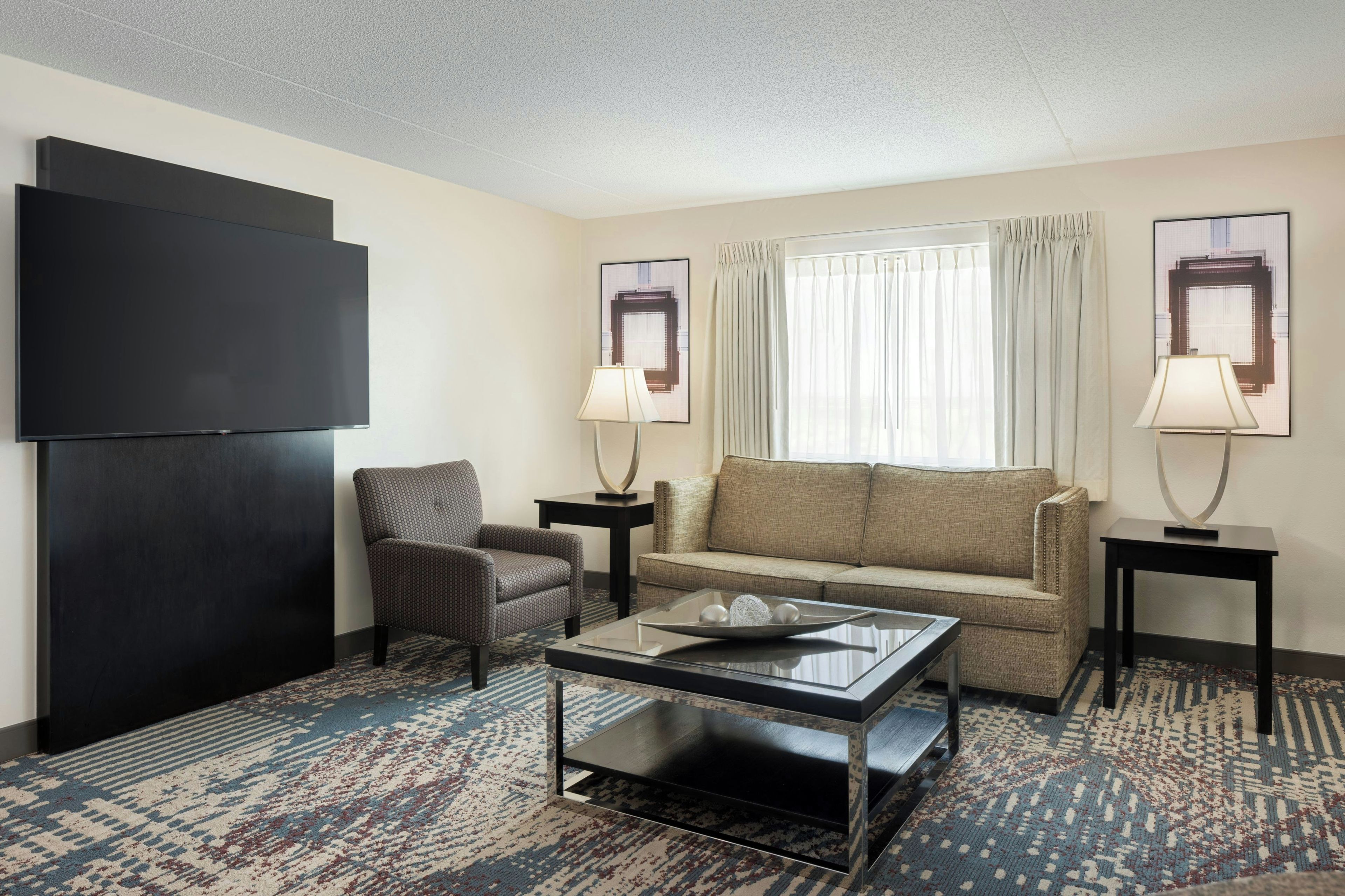 Een hotelkamer met een flatscreen televisie, een bank, een stoel, een salontafel en twee lampen.