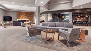 A spacious lobby with a modern sofa, two armchairs, a round coffee table, and a flat-screen TV mounted on the wall.