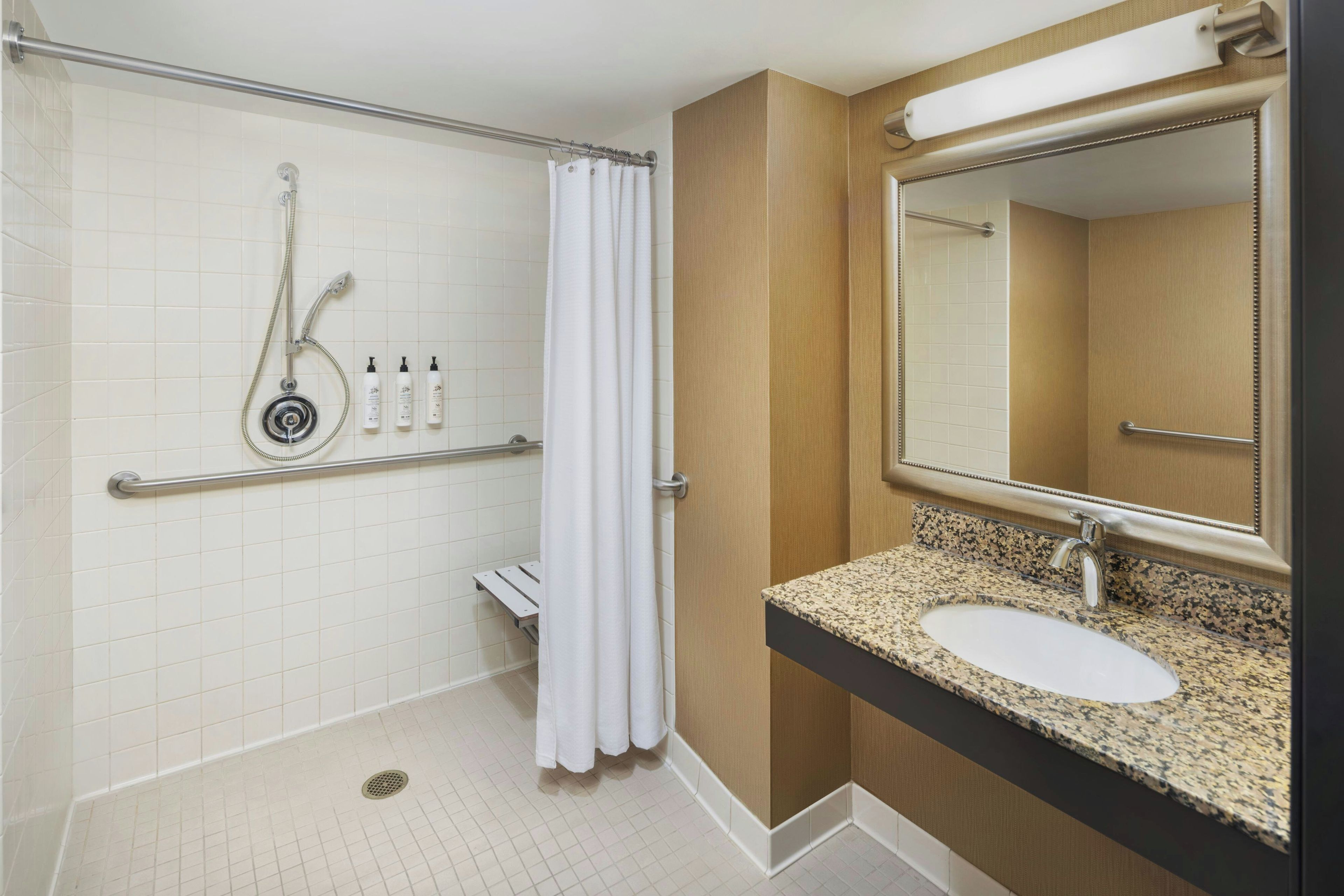 A bathroom with a shower, grab bars, a sink, and a mirror.