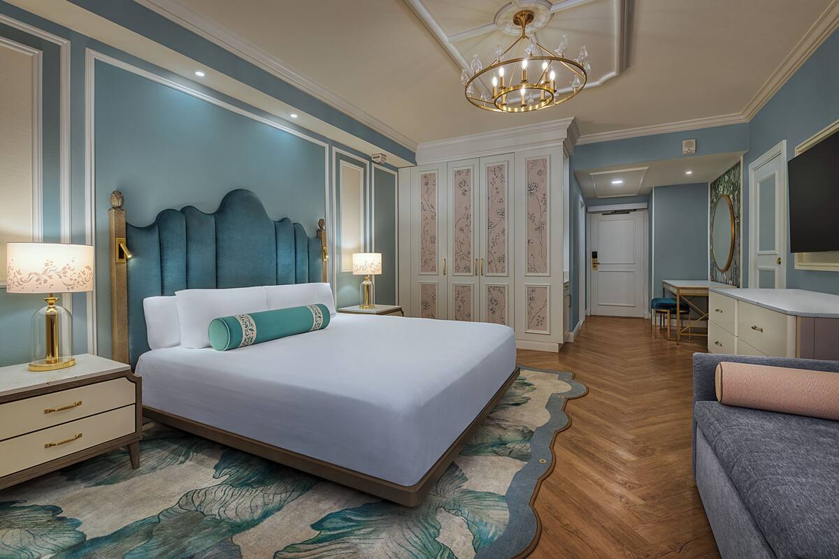 A bedroom with a large bed, nightstands, a chandelier, a desk, and a chair.