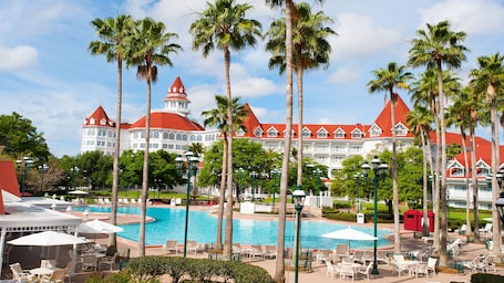 A resort with a large pool, palm trees, and a grand building with red roofs.