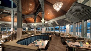 Een ruim restaurant met hoge plafonds, houten balken en grote ramen met uitzicht op de stad.