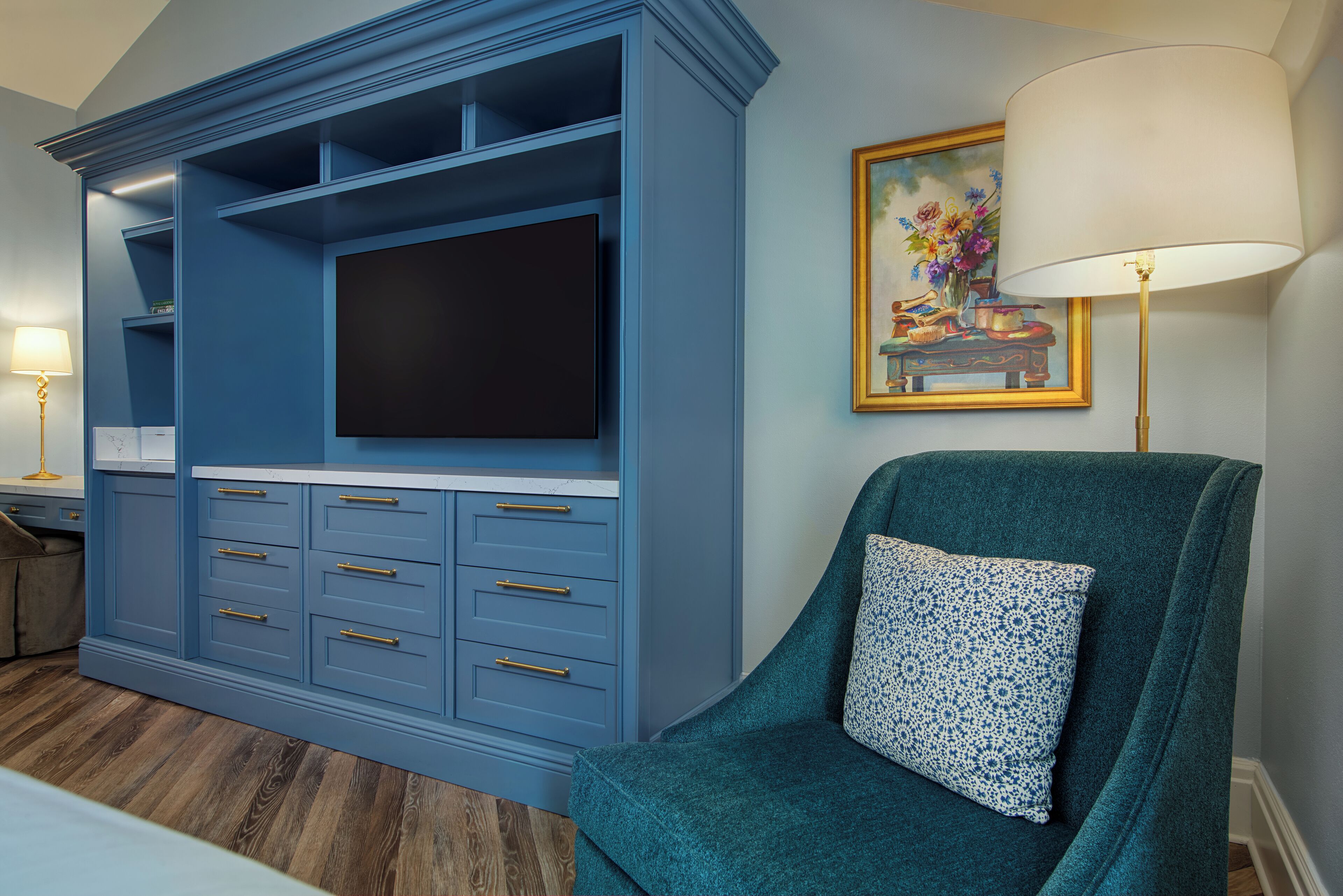 Una habitación con un mueble azul para entretenimiento, un sillón verde azulado y un cuadro en la pared.