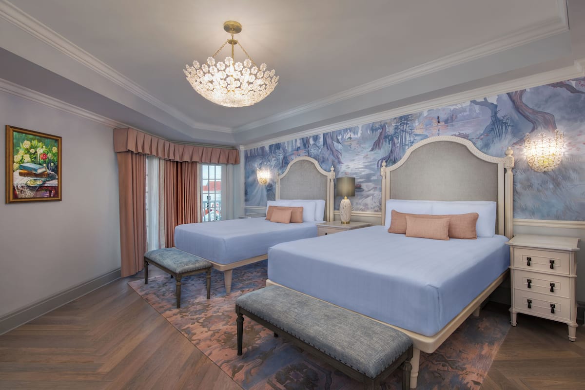 A bedroom with two beds, a bench, a chandelier, and a mural on the wall.