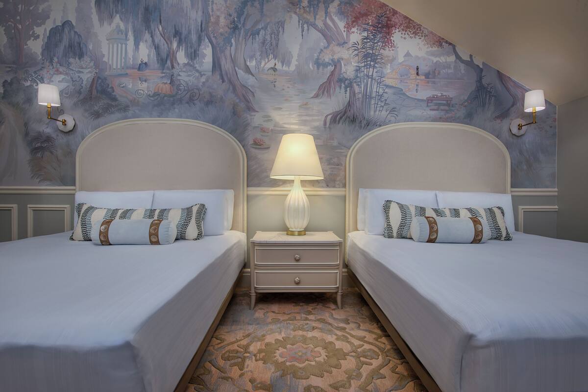 A room with two beds, a nightstand with a lamp, and a mural on the wall.