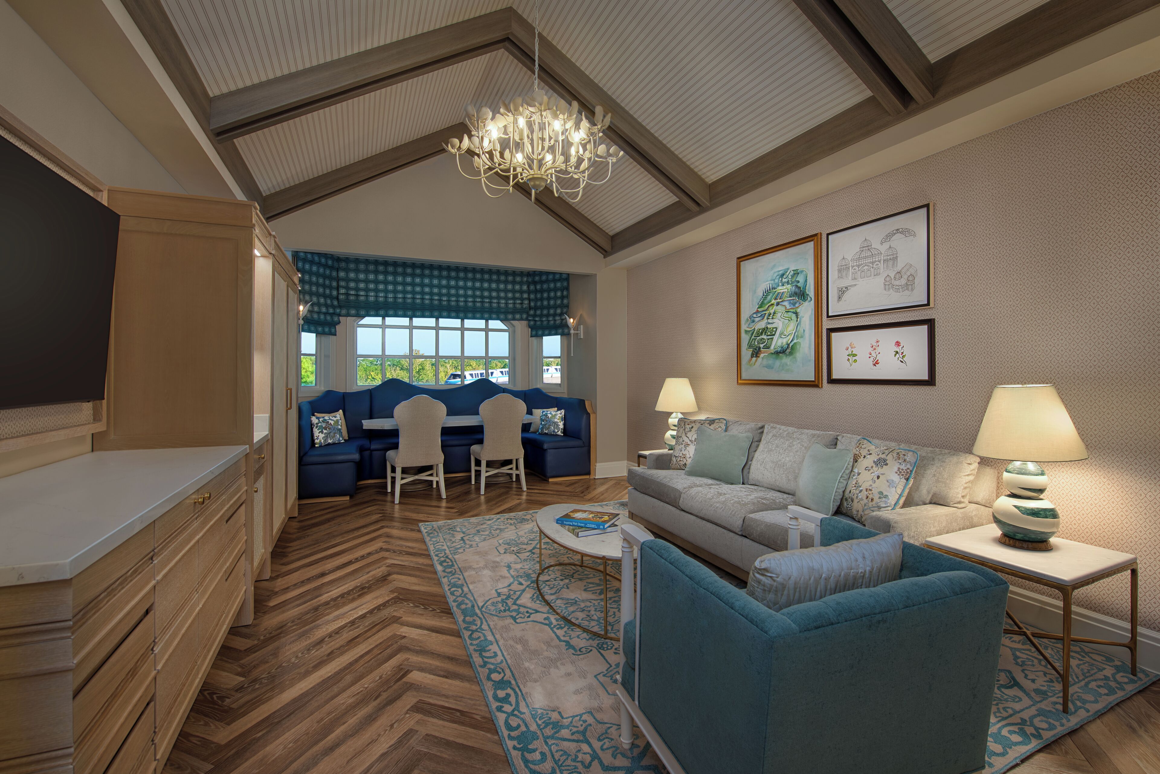 A modern living room with a blue sofa, a coffee table, and a chandelier. There is a dining area with a blue table and chairs.
