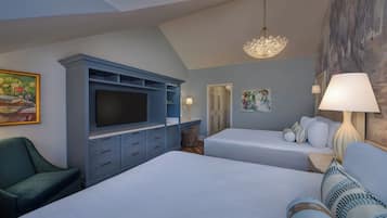 Quarto de hotel com uma cama grande, uma televisão sobre um móvel azul, uma cadeira, duas mesas de cabeceira com luminárias e obras de arte nas paredes.
