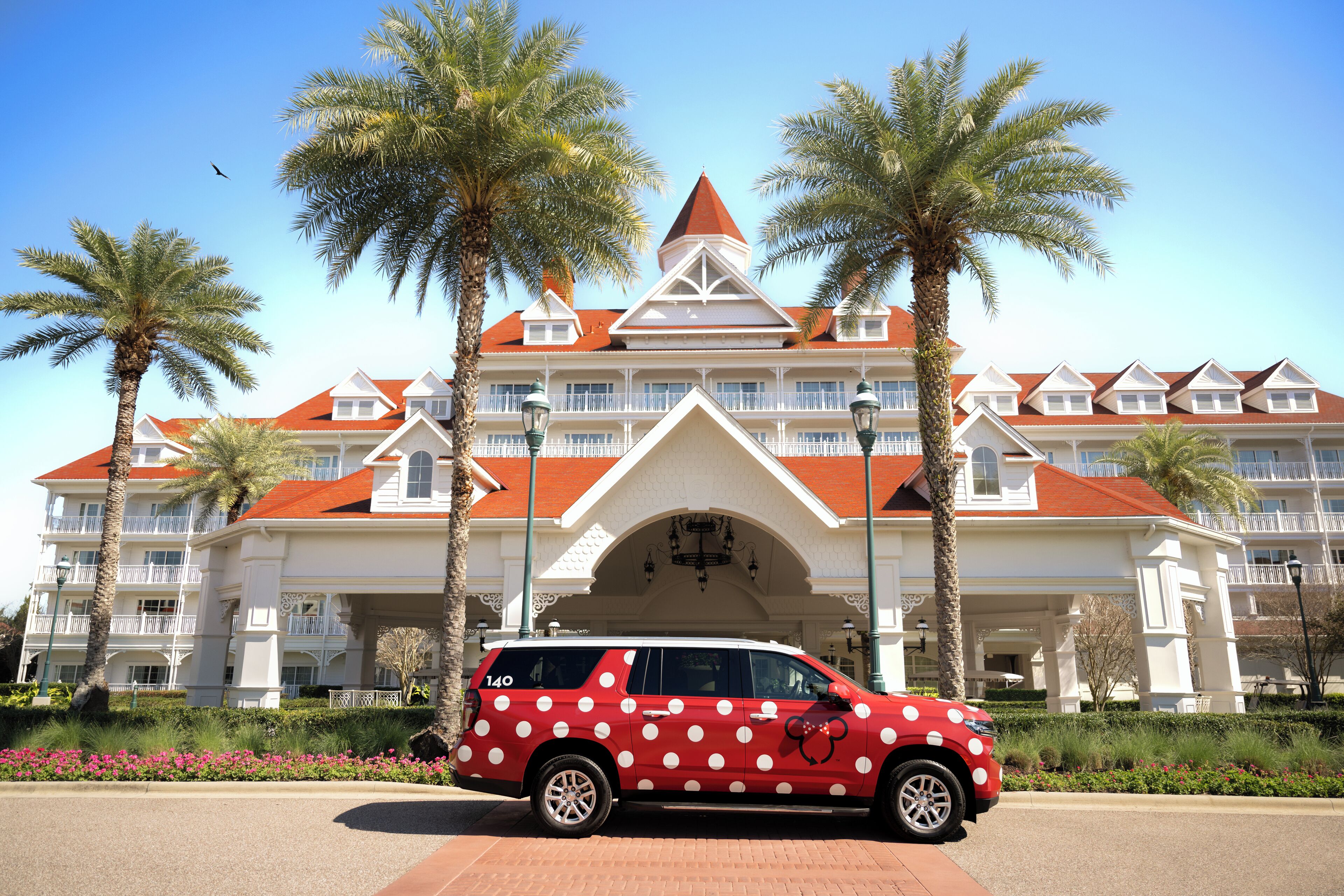 Un hotel con techo rojo, balcones blancos y palmeras.