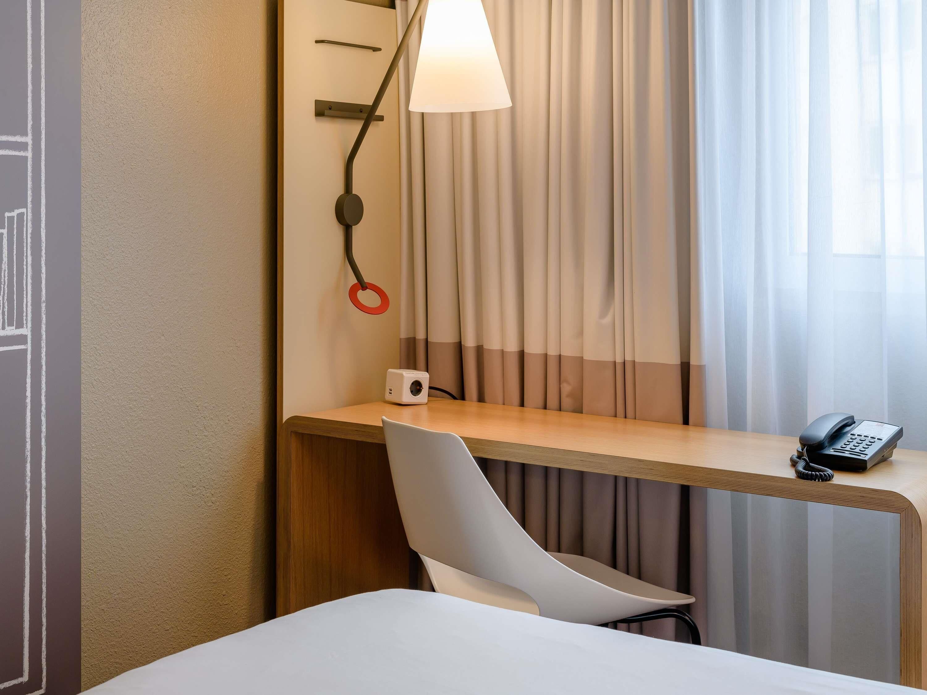 Ein Hotelzimmer mit Schreibtisch, Lampe, Telefon und Stuhl.