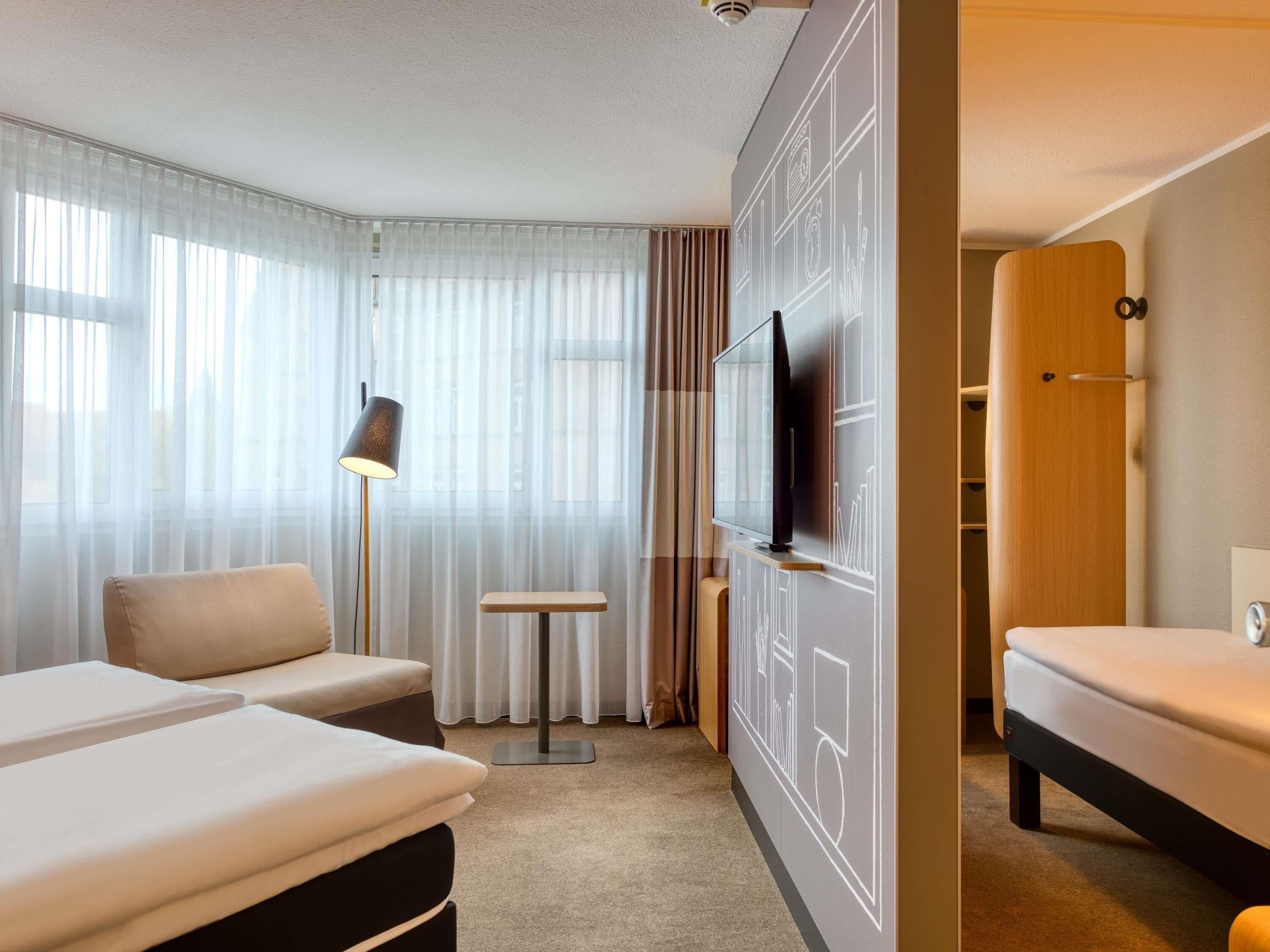 Ein Hotelzimmer mit zwei Betten, einem Fernseher, einer Lampe, einem kleinen Tisch und einem Kleiderschrank.