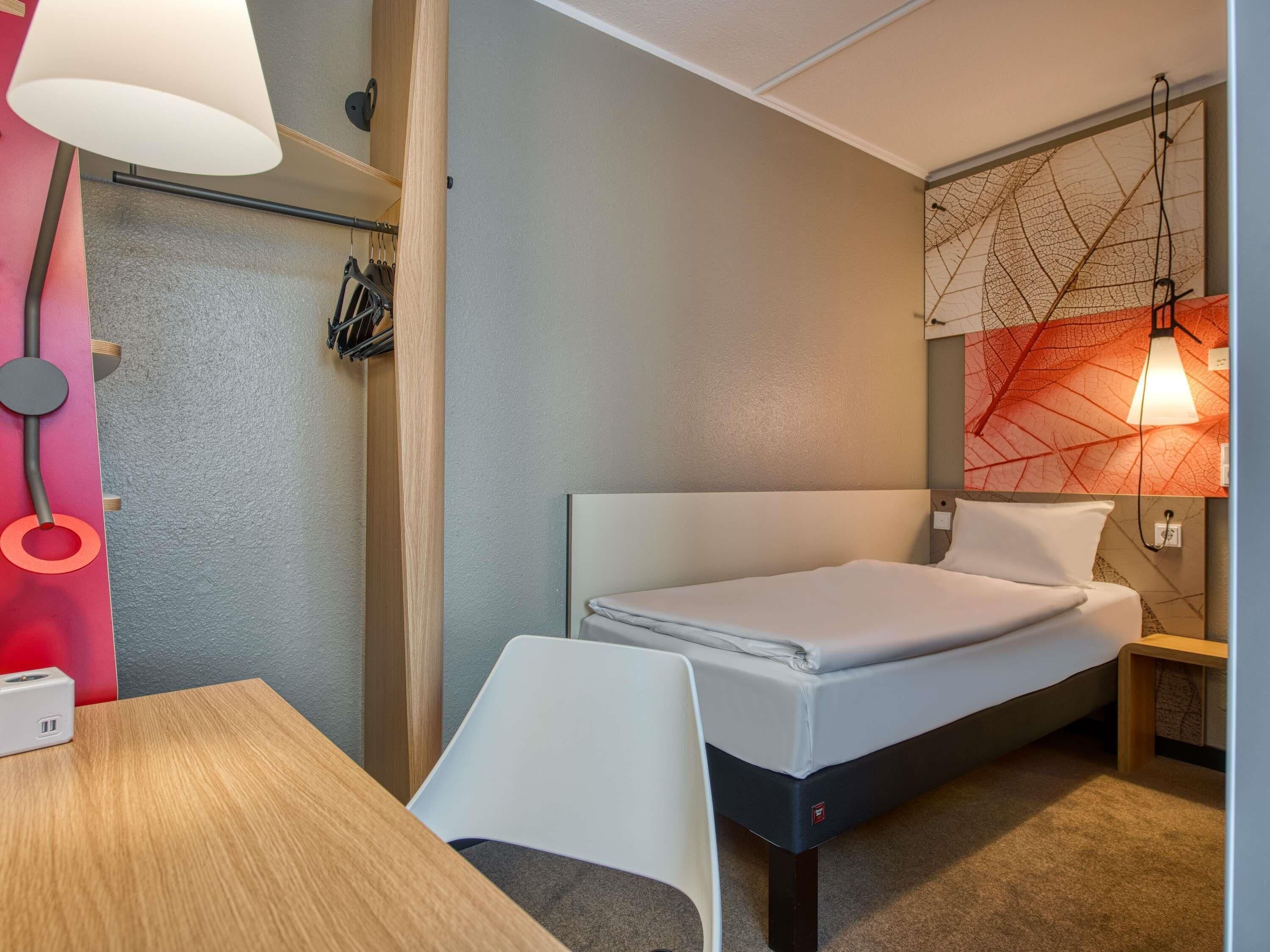 Ein kleines Hotelzimmer mit einem Einzelbett, einem Schreibtisch und einem Stuhl.