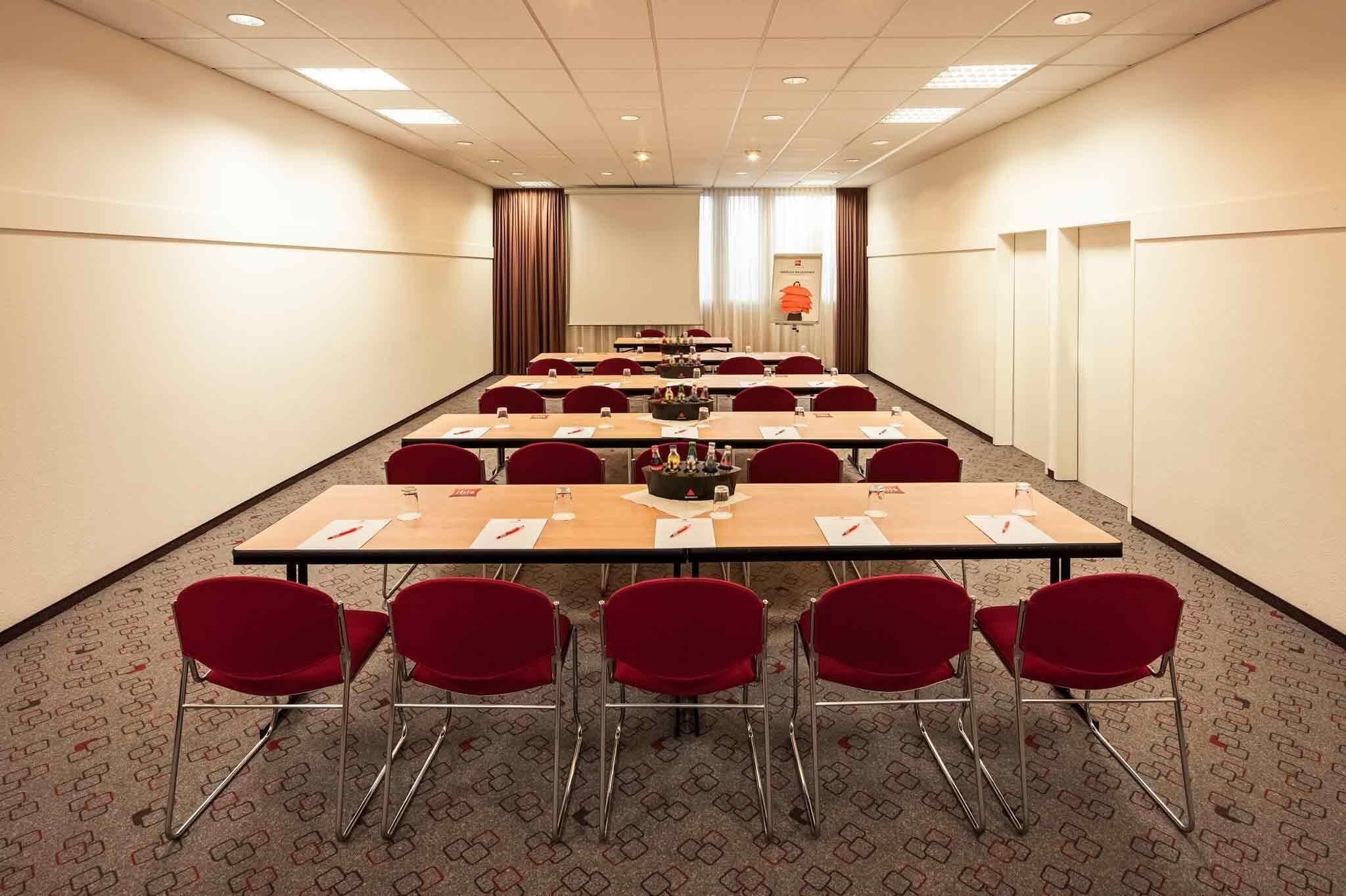 A conference room with long tables, red chairs, and a carpeted floor.