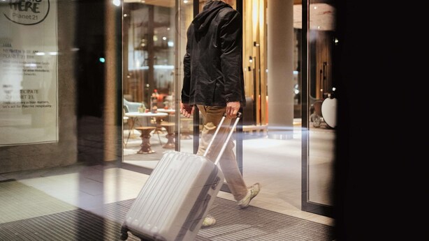 A man walking through a hotel entrance with a suitcase, a glass door, and a sign with text. - ibis Nuernberg City am Plaerrer (Nuremberg)
