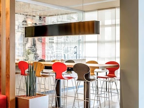 Uma sala de jantar moderna com uma mesa comprida, cadeiras vermelhas de madeira e um lustre pendurado.