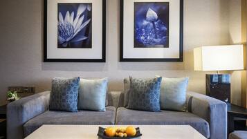 A modern living room with a grey sofa, two patterned throw pillows, a coffee table with fruit, and two framed wall art pieces.