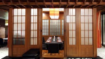 A traditional Japanese-style room with tatami flooring, a low table set with plates and chopsticks, and sliding doors with frosted glass panels.