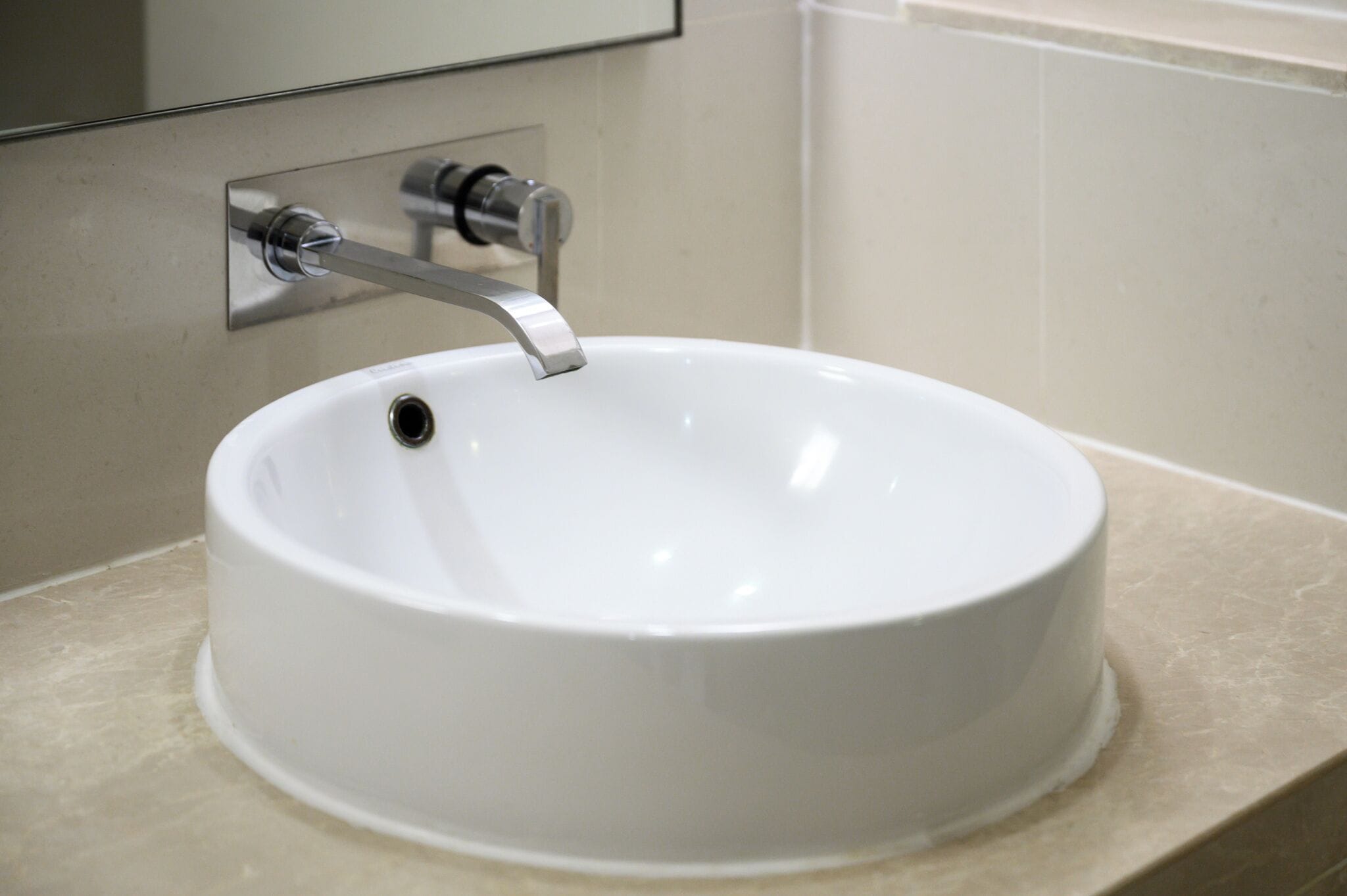 Un lavabo de cerámica blanca con un grifo moderno instalado sobre una encimera color beige.