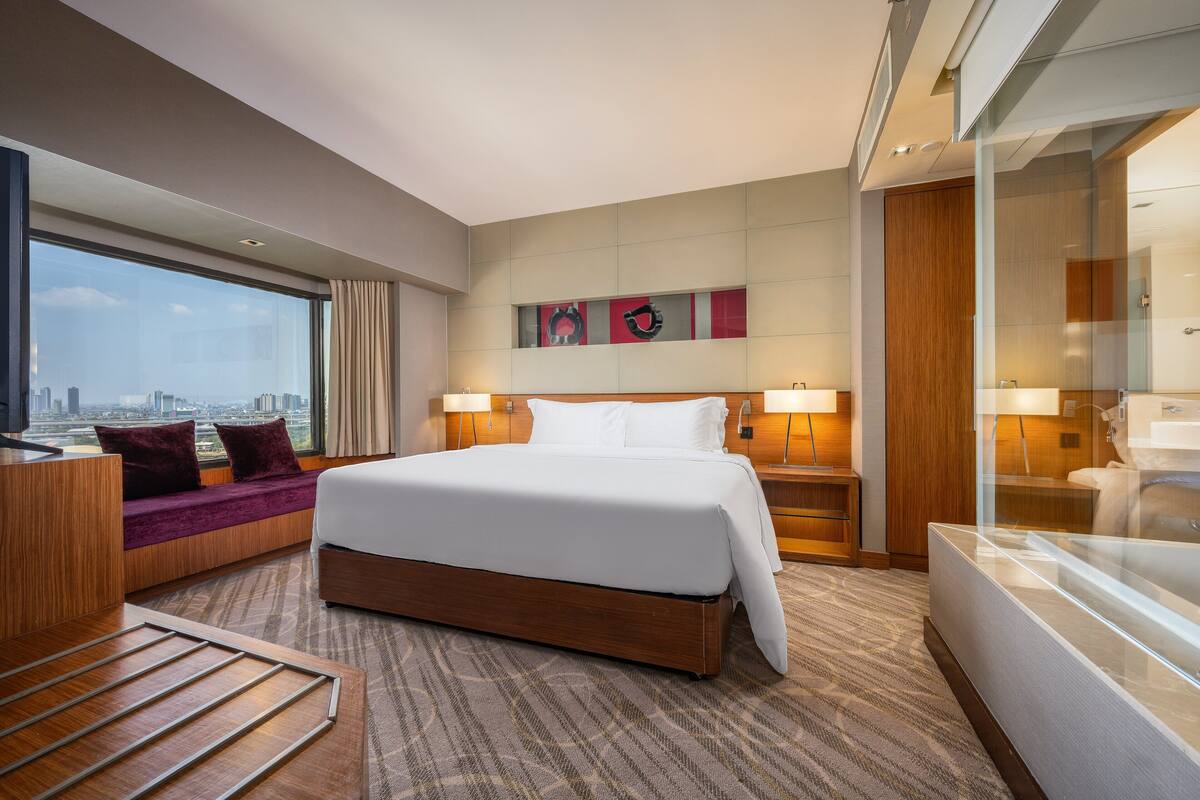 Ein Hotelzimmer mit einem großen Bett, einer Sitzecke mit Blick und einer Stadtansicht durch das Fenster.
