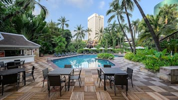A pool area with lounge chairs and a dining area with tables and chairs.