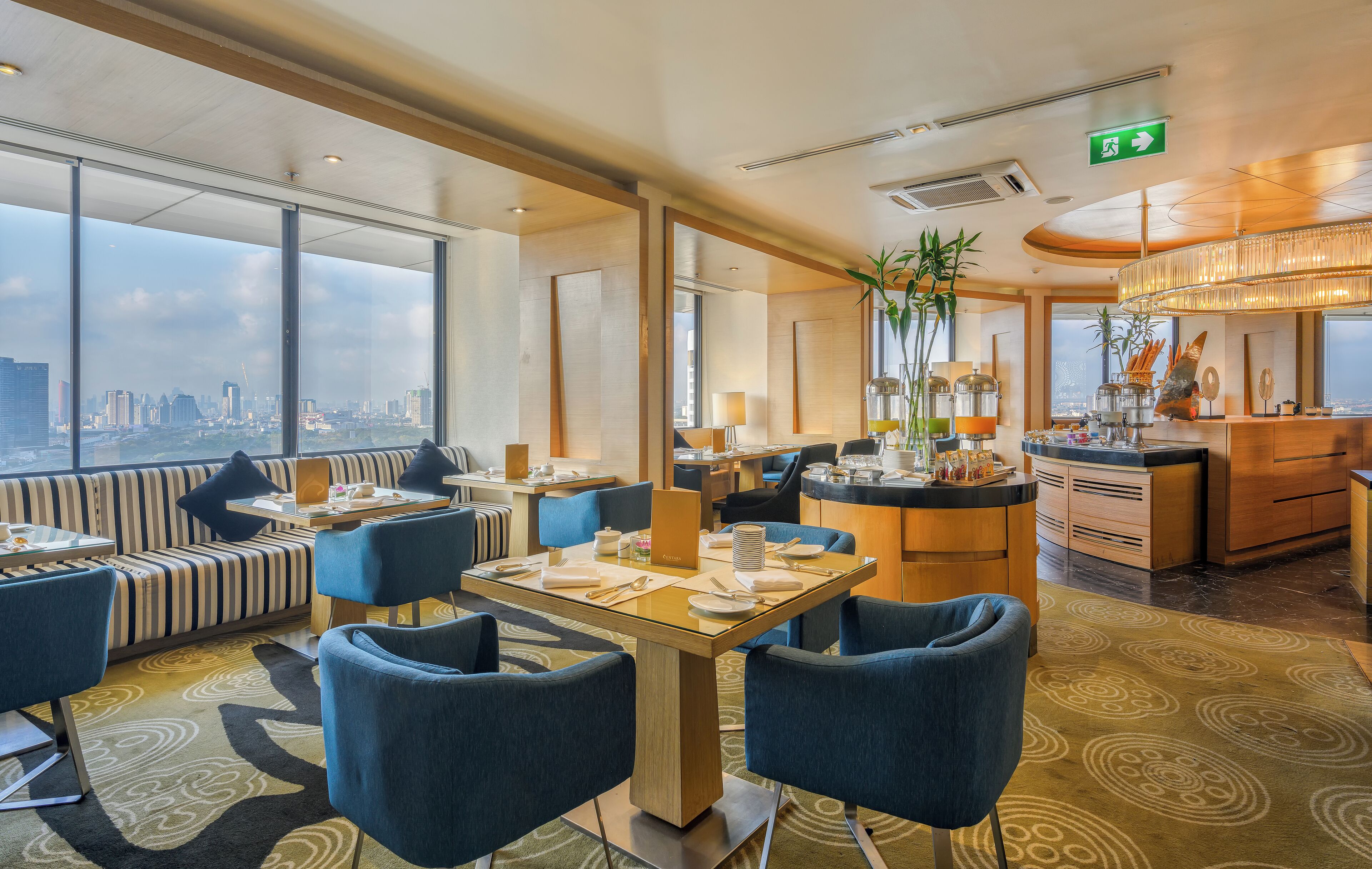 Un comedor moderno de hotel con vistas a la ciudad, con mesas y sillas dispuestas, y una zona de bar.