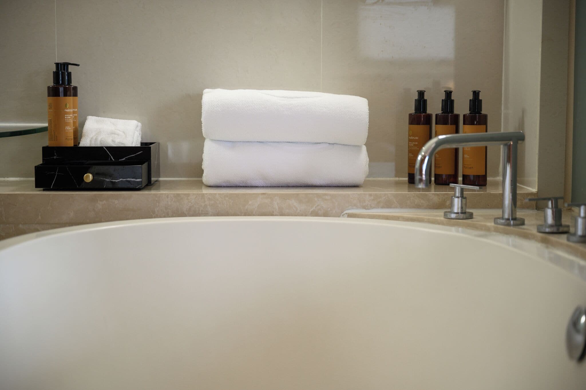 A bathroom with a large bathtub, a towel rack with folded towels, and toiletries on the counter.