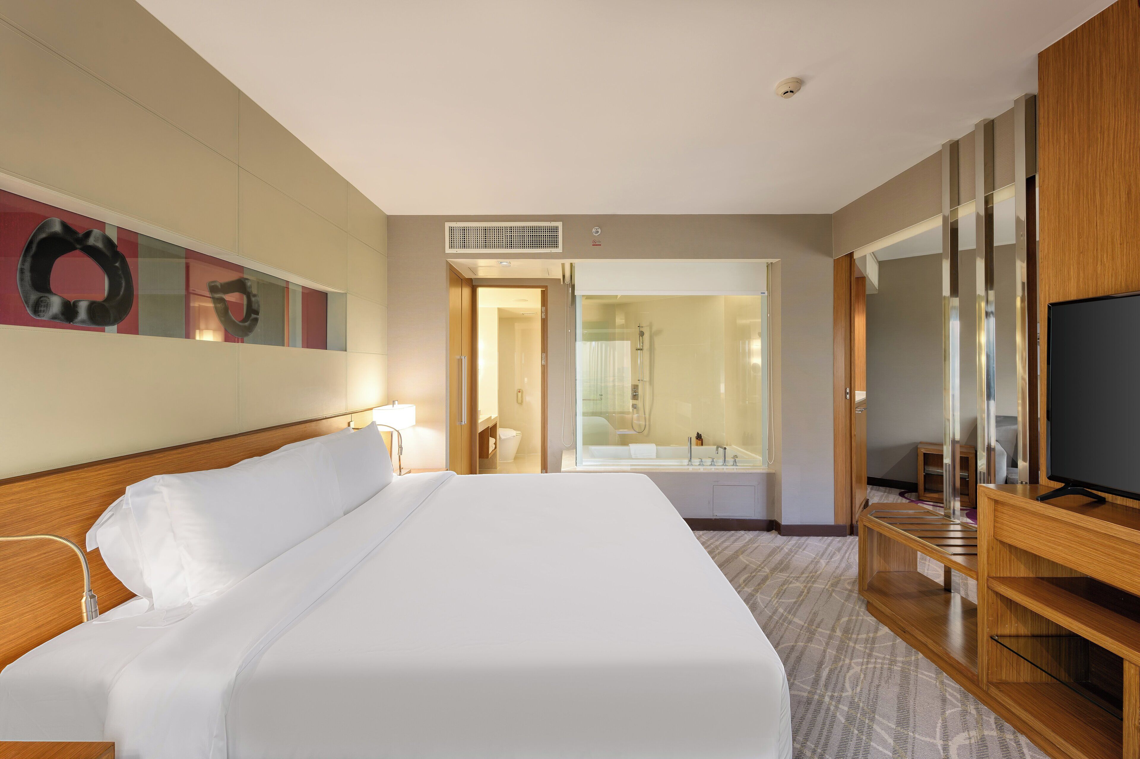 A hotel room with a large bed, a television, a wooden desk, and a bathroom visible through an open door.