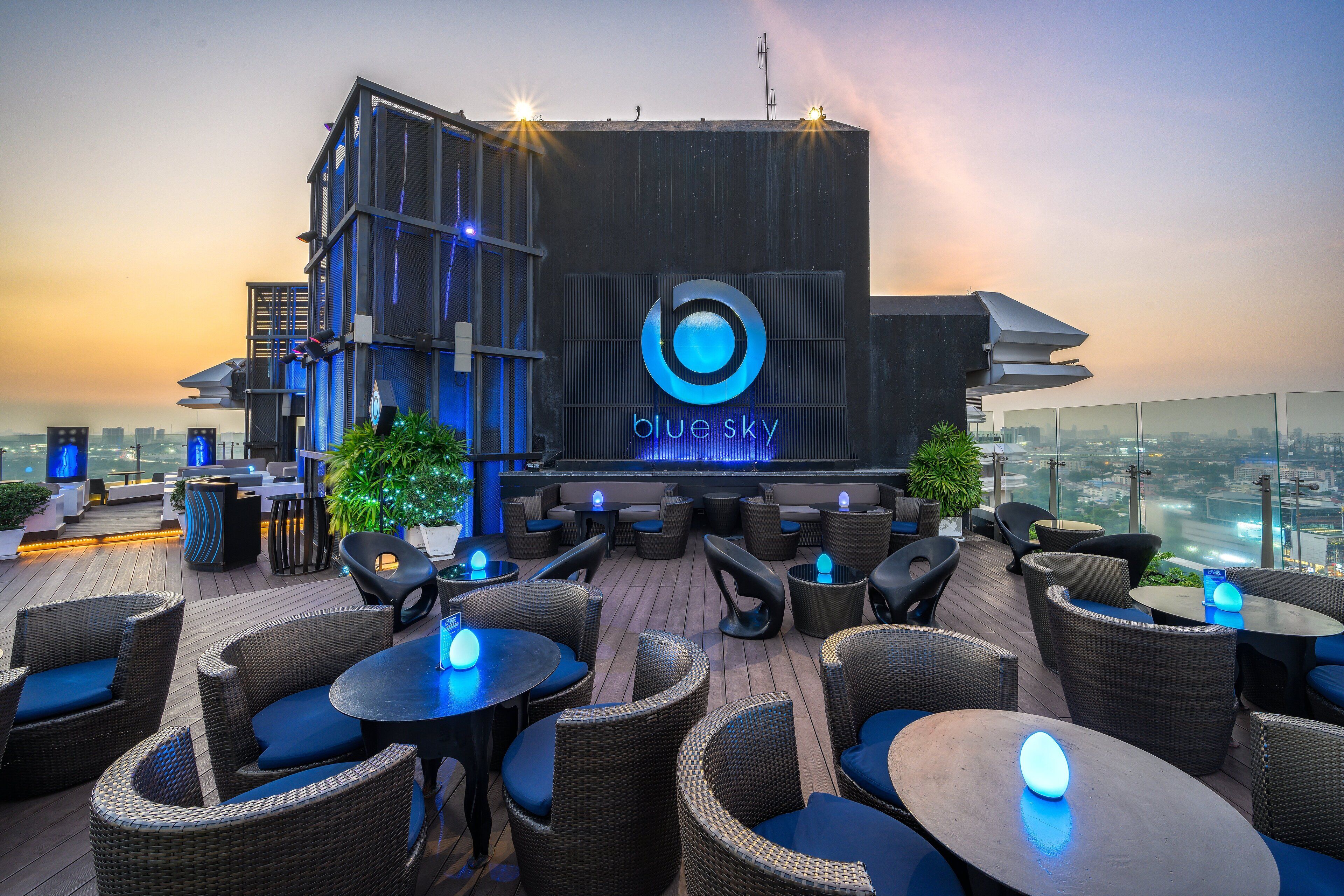 A rooftop bar with wicker furniture and a large illuminated logo.