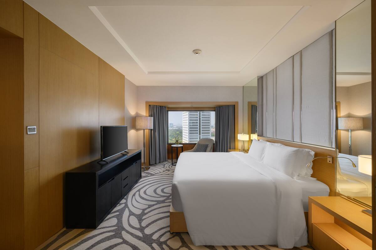 Ein Hotelzimmer mit einem großen Bett, einem Fernseher auf einer Kommode, einem Schreibtisch mit Stuhl und Blick auf die Stadt.