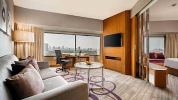 A modern hotel room with a sofa, a desk, a flat-screen TV, and a city view.