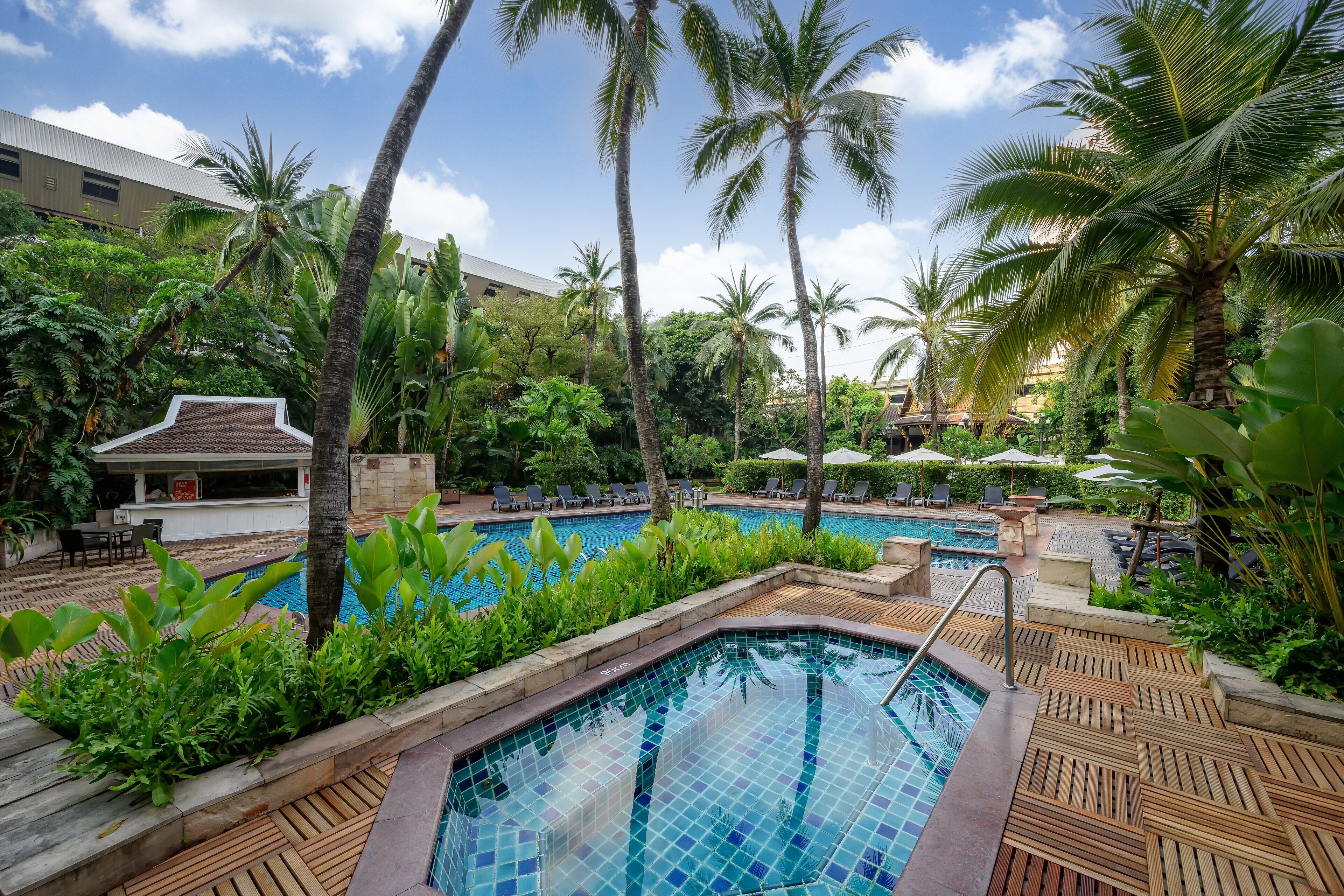 A pool area with wooden decking, palm trees, and lounge chairs.