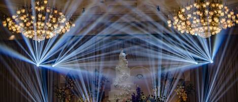 A multi-tiered wedding cake with floral decorations, surrounded by a chandelier and light beams.