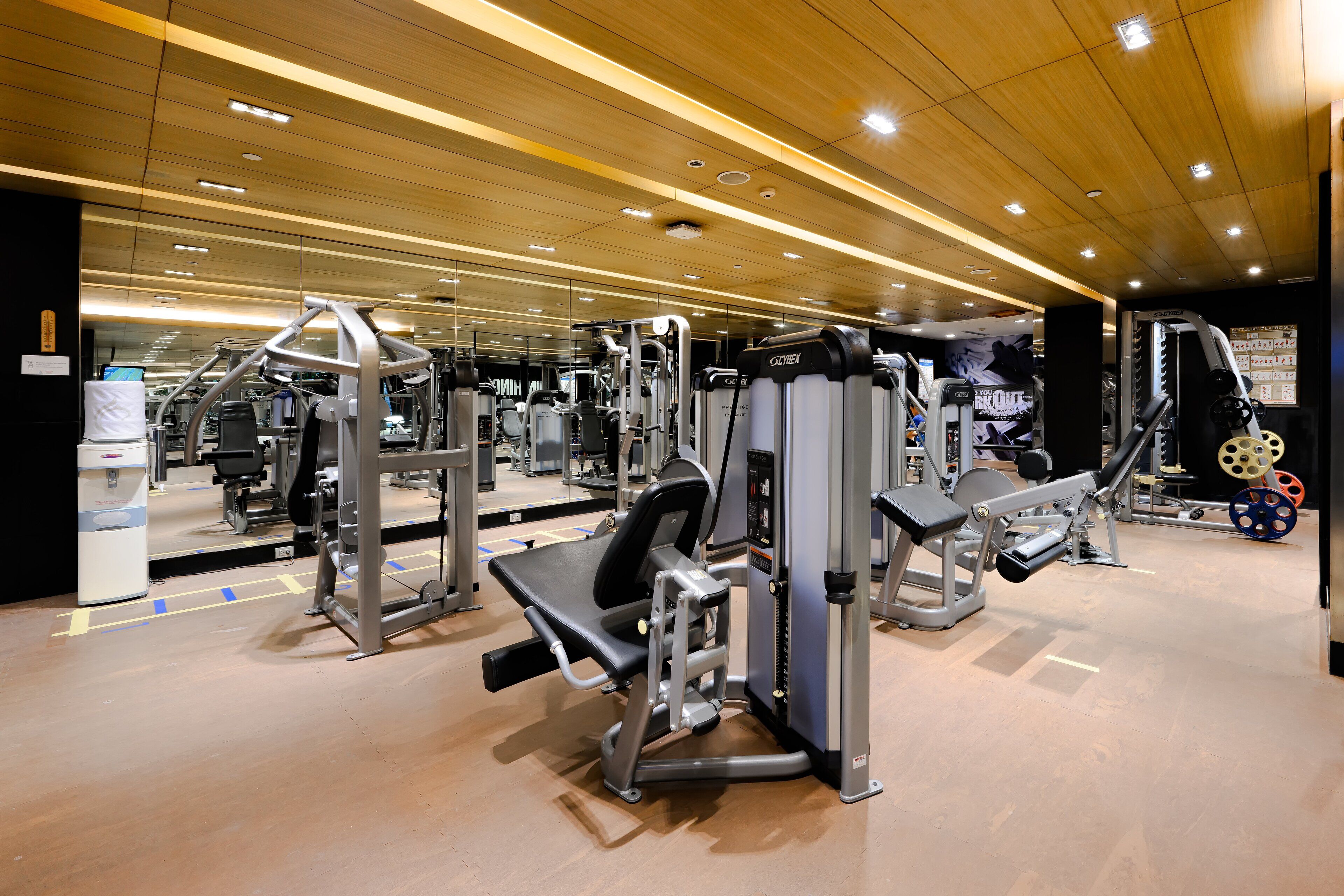 A gym with various exercise machines, a mirror wall, and a wooden ceiling.