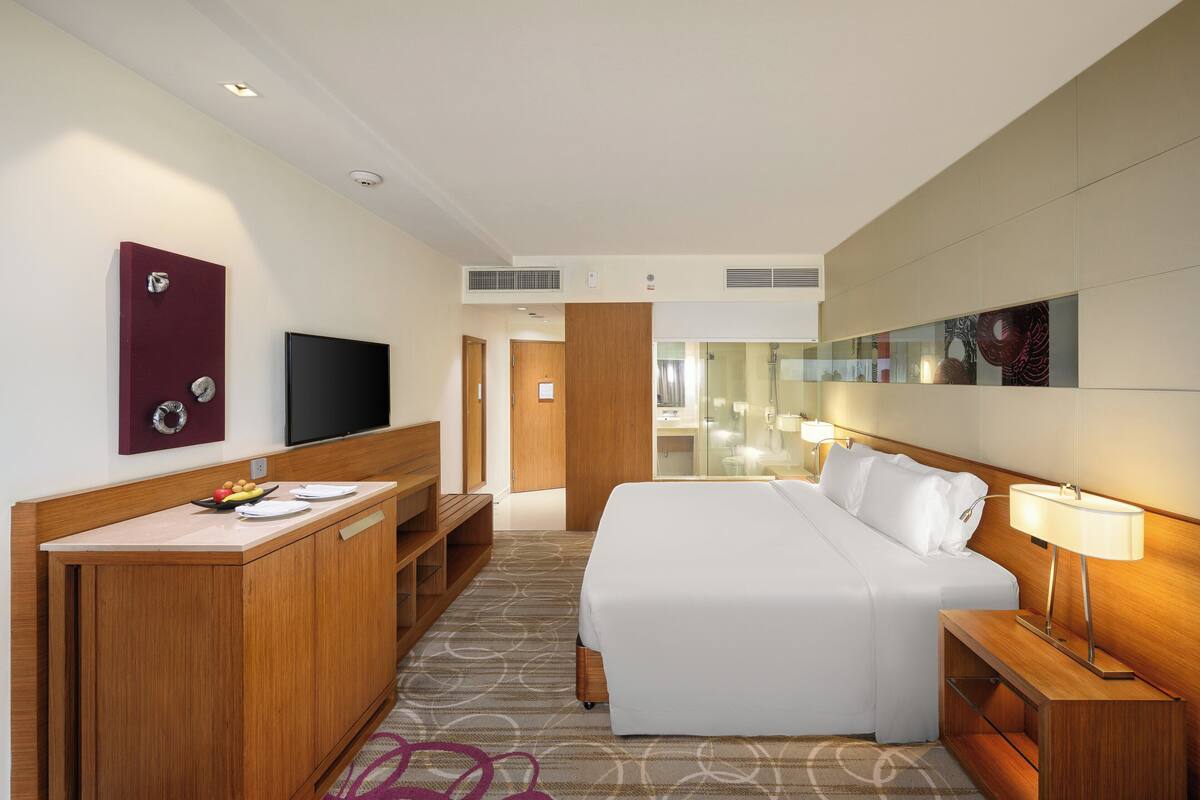 Ein Hotelzimmer mit einem Bett, einem Schreibtisch mit Flachbildfernseher, einer Holzkommode und einem Spiegel an der Wand.