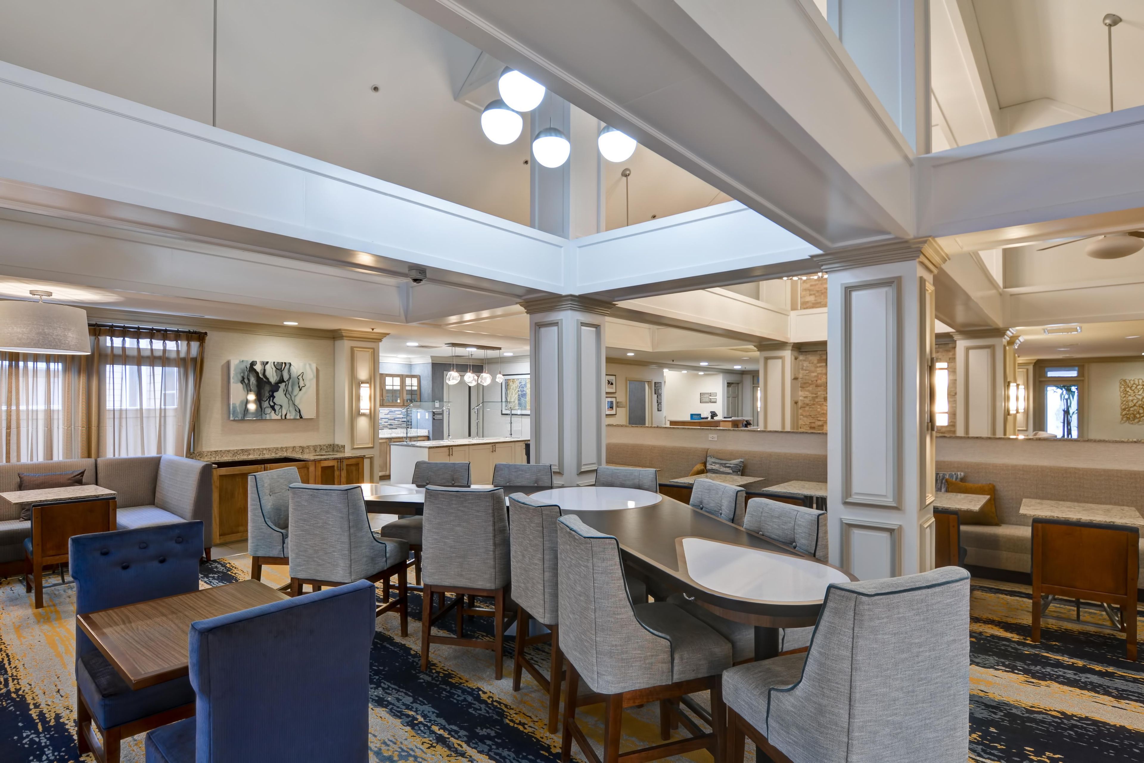 Une salle à manger d’hôtel avec plusieurs tables et chaises, une cuisine à l’arrière-plan et un grand miroir au mur.