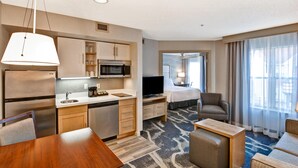 Een hotelkamer met een kitchenette, een bed, een televisie, een zithoek en een groot raam.