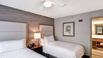 A hotel room with two beds, a ceiling fan, a nightstand, a lamp, and a framed picture on the wall.