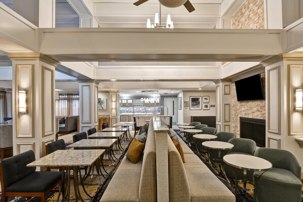 Un vaste espace de restauration dans l’hôtel, offrant de nombreuses options de sièges, notamment des tables et des bancs, avec une cuisine située à l’arrière-plan.