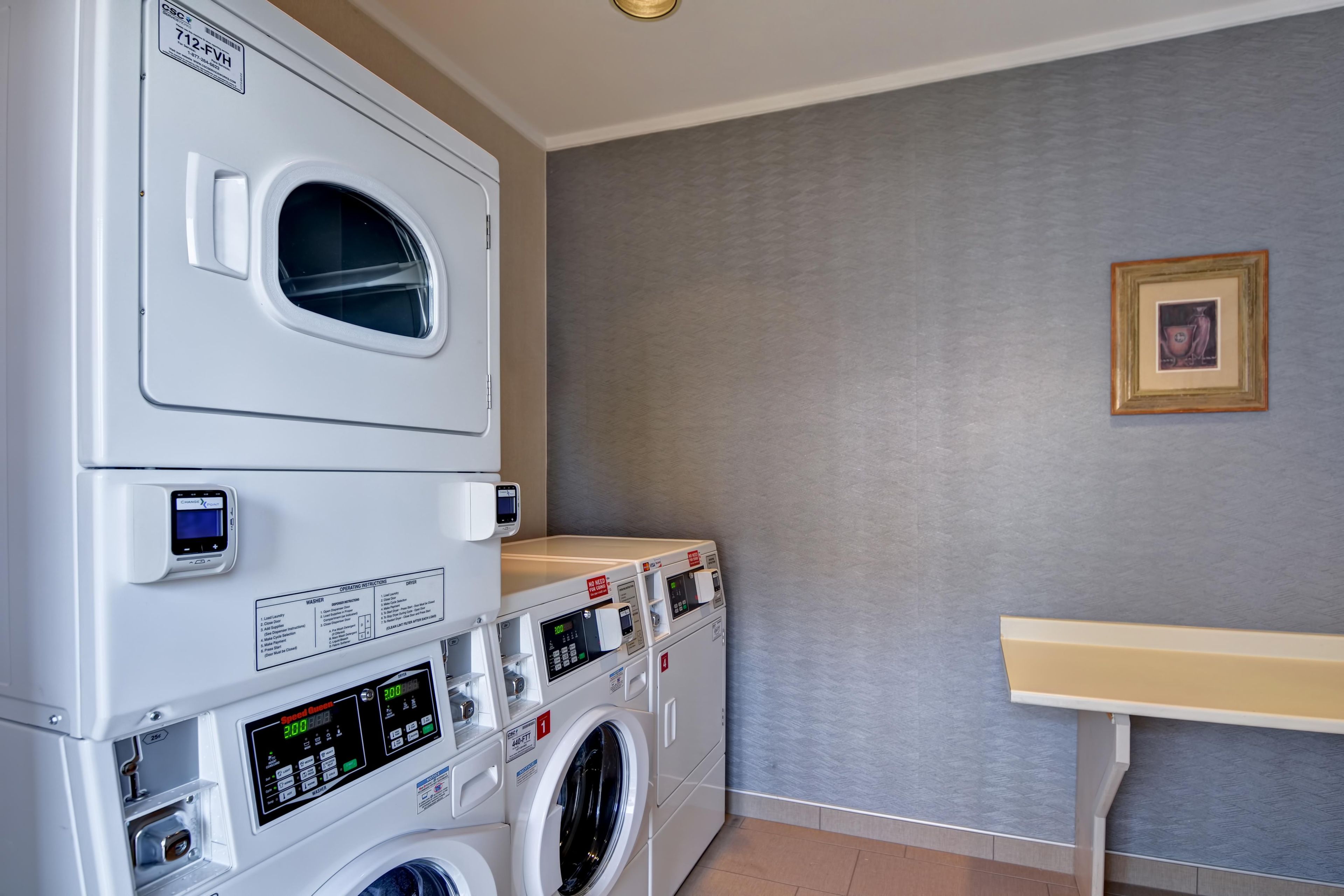 A laundry room with stacked washers and dryers, a control panel, and a small table.